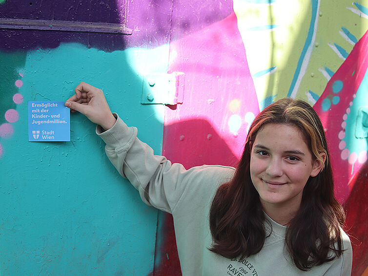 Eine Jugendliche bringt einen Sticker an den Waggon mit der Aufschrift "Ermöglicht mit der Kinder- und Jugendmillion"