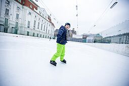 Ein Junge mit grellgrüner Hose am Eislaufplatz.