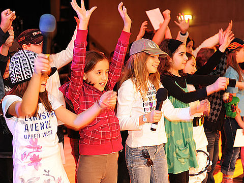 Kinder singen und strecken die Hände in die Höhe