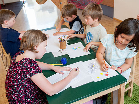 Kinderbetreuung in Wien finden! Kindergartenkinder sitzen rund um Tisch und zeichnen.