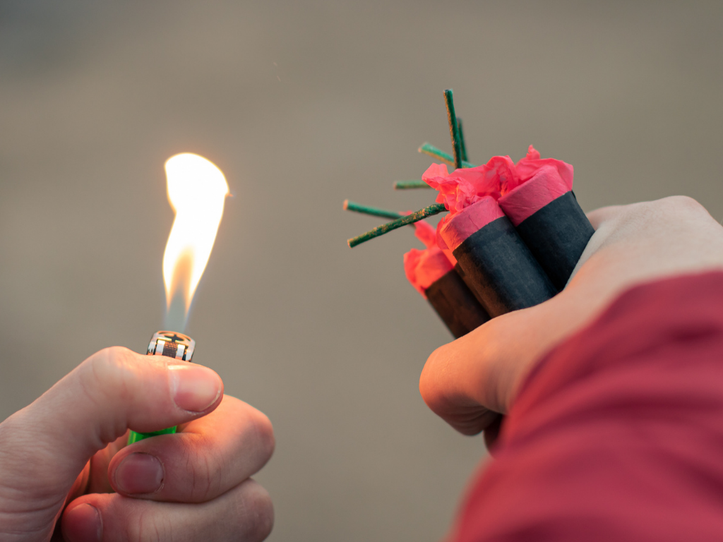 Eine linke Hand mit Feuerzeug und in der rechten Hand sind Böller bzw. Feuerwerkskörper.