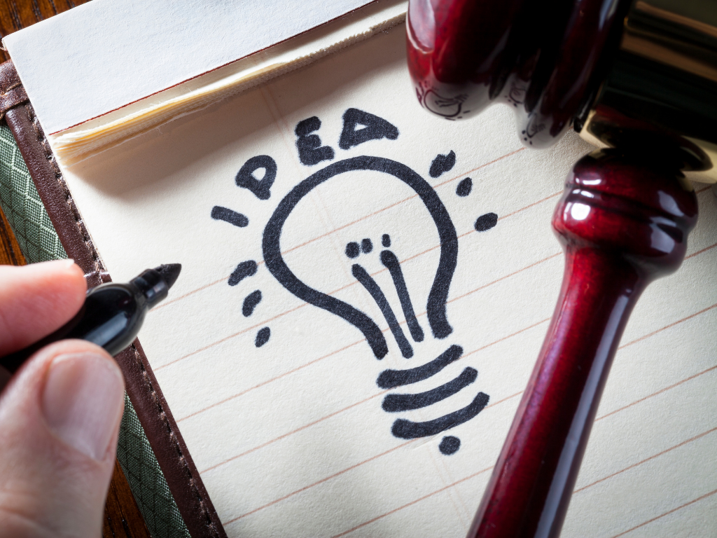 Ein Zettel auf eine Glühbirne gemalt wurde und auf dem ein Richterhammer liegt