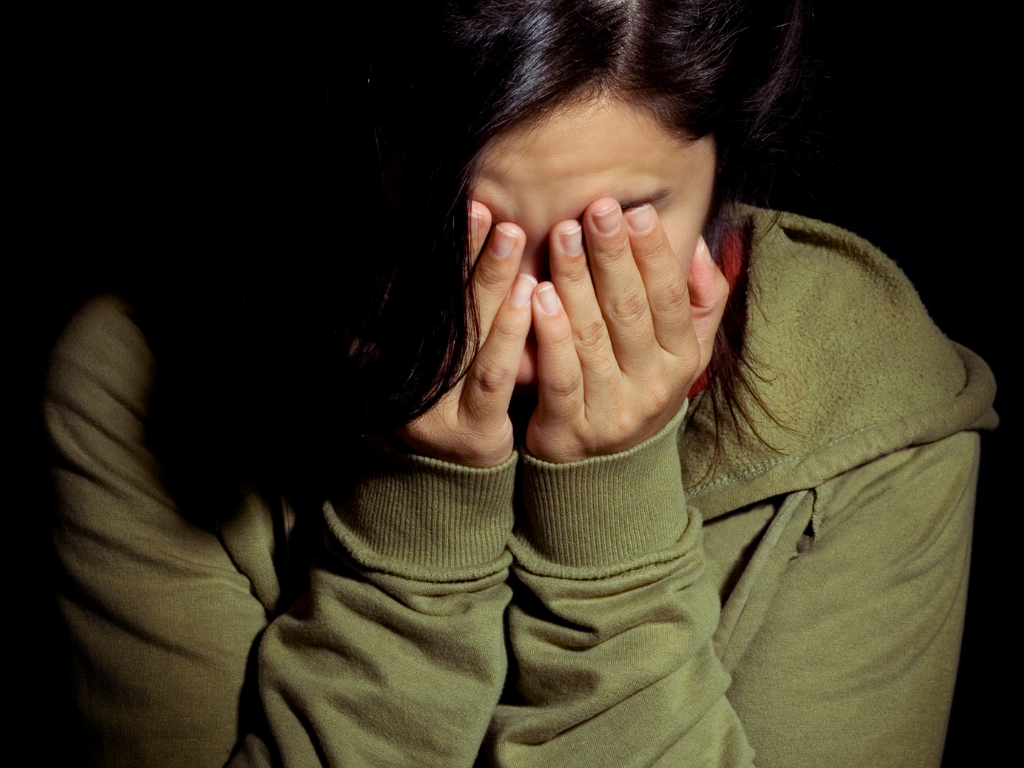 eine Person mit grünen Pullover schlägt ihre Hände vor dem Gesicht zusammen