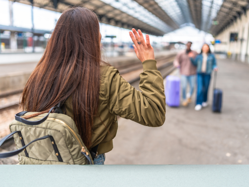 Eine Person winkt zwei anderen Personen mit Koffern zu