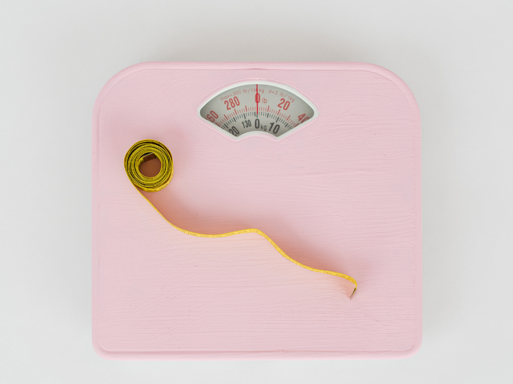 eine rosa Körperwaage auf der ein gelbes Maßband liegt