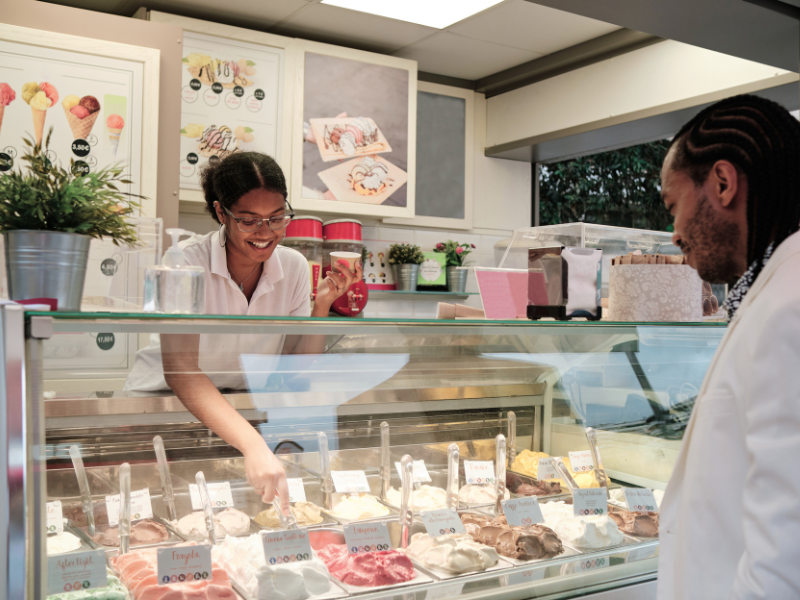 Eine Person verkauft einer anderen Person ein Eis am Eisstand