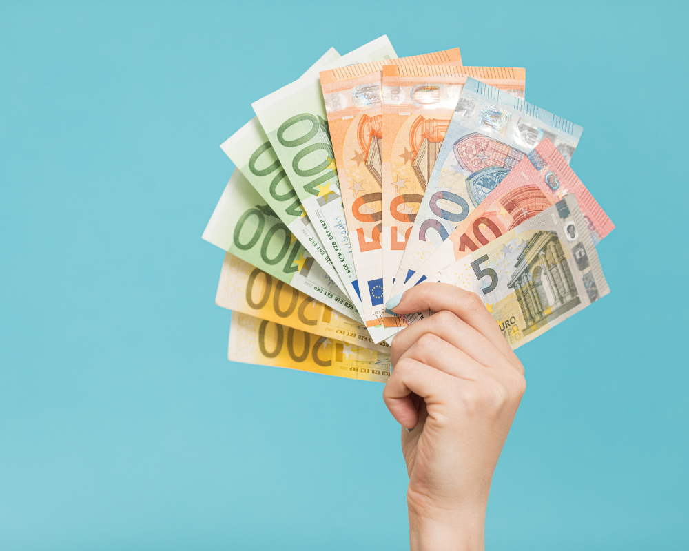 Eine Hand hält viele Geldscheine in die Höhe vor einem blauen Hintergrund