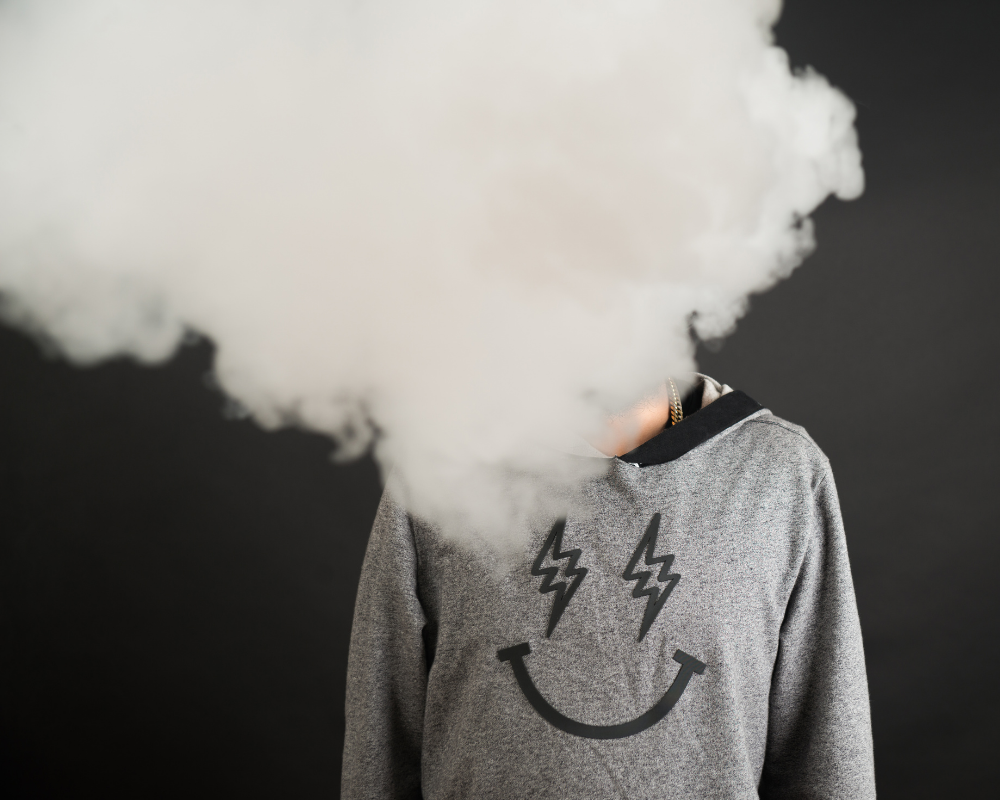 eine Person steht vor dunklem Hintergrund und eine Rauchschwade verdeckt den Kopf