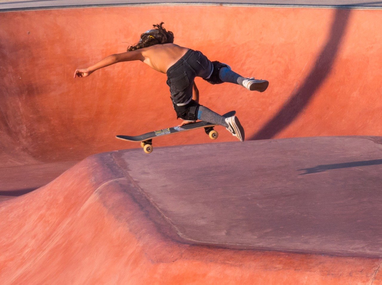 Eine Person skatet in einer orange-braunen Halfpipe und führt einen Trick aus, die Arme zum Balancieren ausgestreckt.