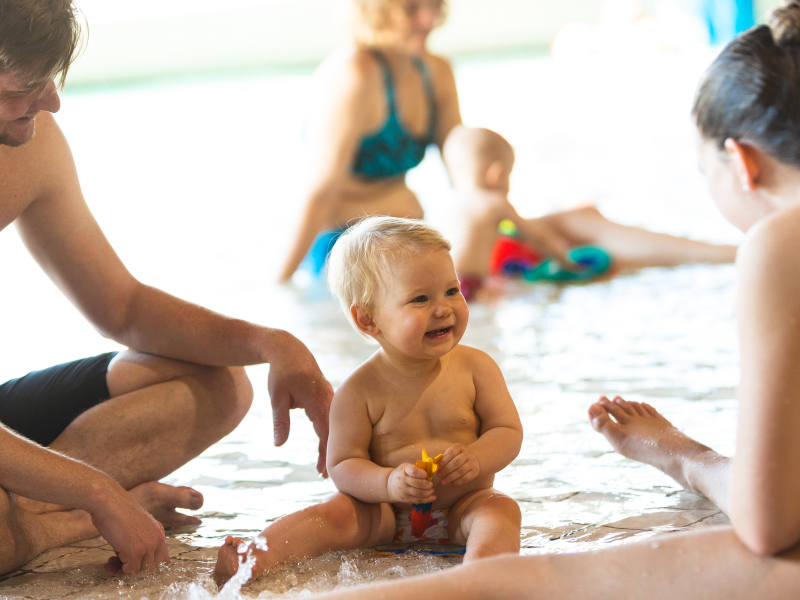 Ein Baby sitzt im Schwimmbad und lacht.