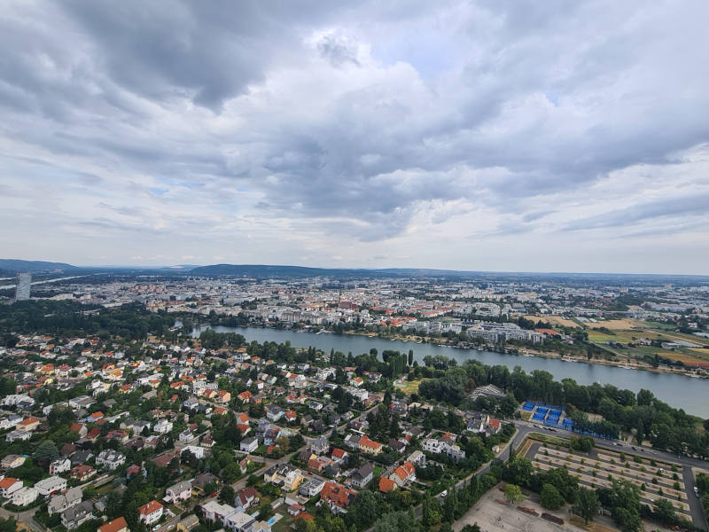 AussichtDonauturm Aussicht vom Donauturm: im Vordergrund viele Bäume, vereinzelt Häuser, danach horizontal die Donau, dahinter viele Miniaturhäuser.