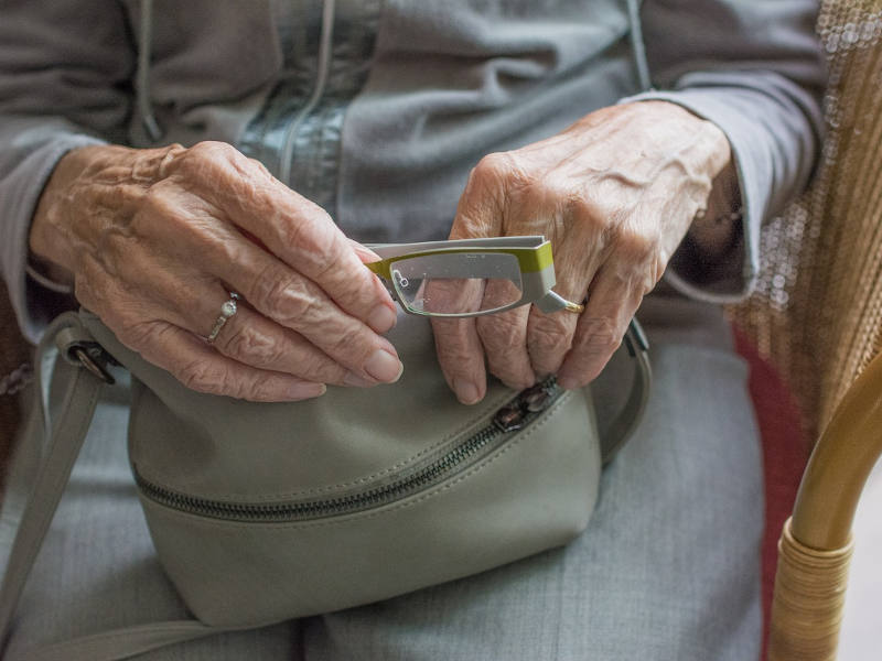 Nahaufnahme von älteren Händen mit einer Brille.