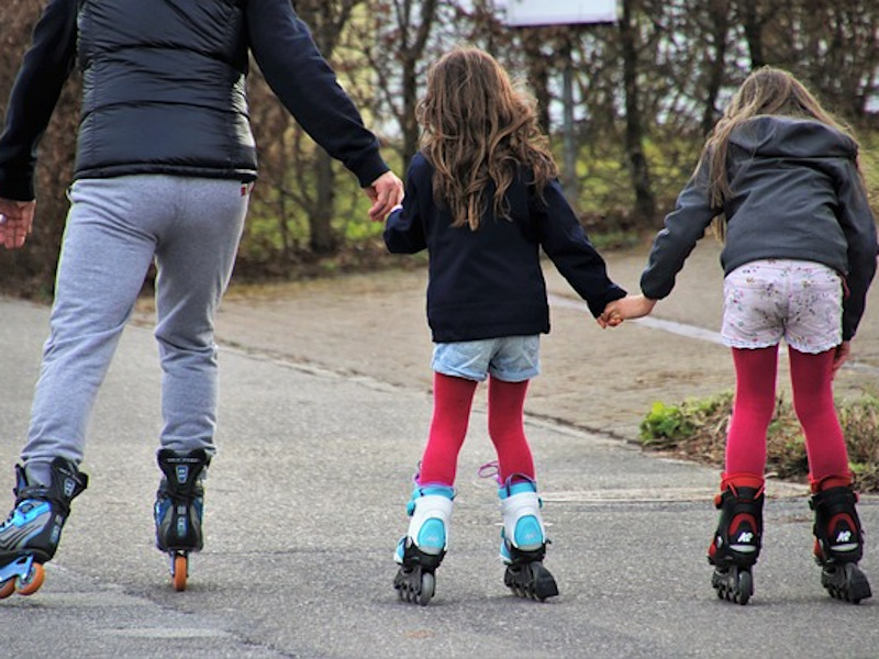 Erwachsene Person und 2 Mädchen tun Hand in Hand Inline Skaten