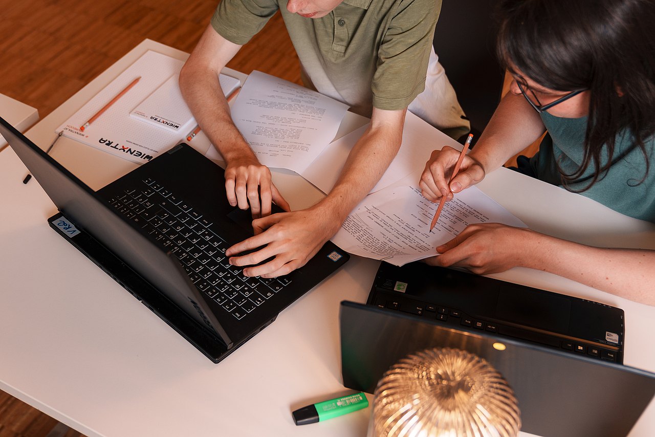mz2025 x ste.krenn-141 Zwei Personen sitzen an einem Tisch und arbeiten mit Laptops und Zetteln.