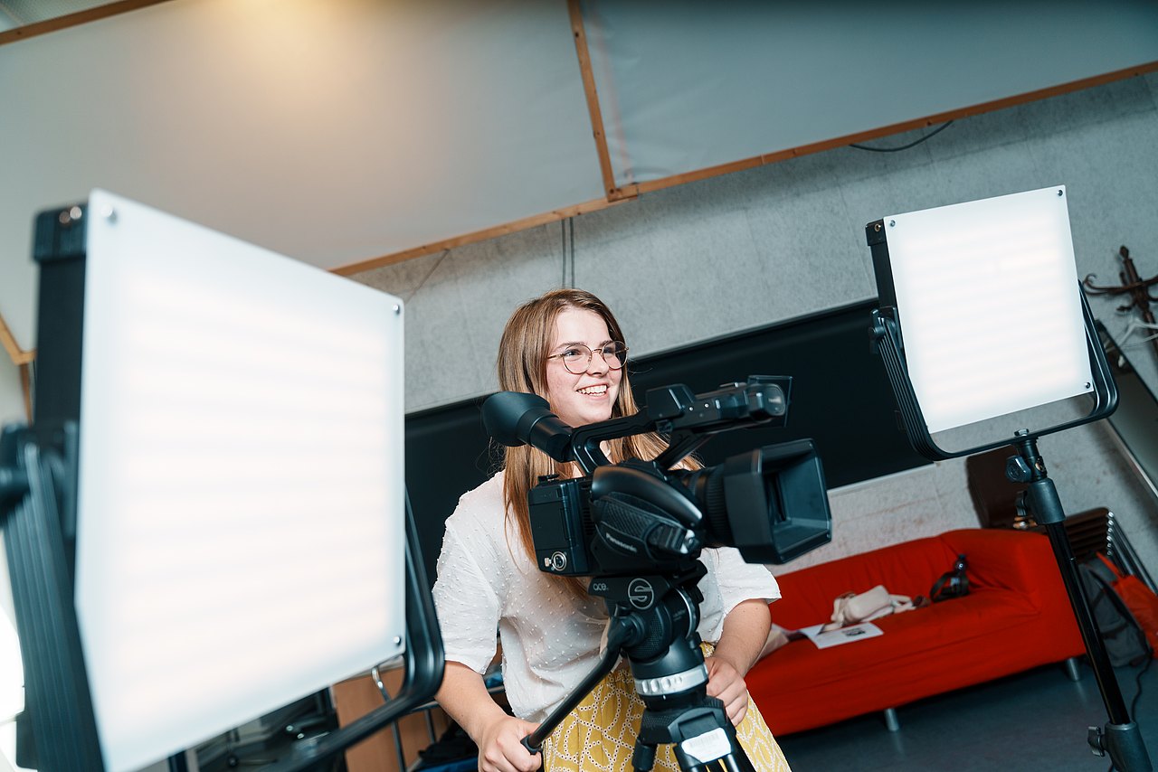 mz2025 x ste.krenn-32 Eine Jugendliche steht zwischen zwei Videoleuchten und bedient Panasonic-Videokamera.