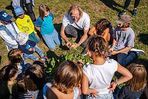 Kinder stehen mit Workshopleitung im Kreis um geerntetes Gemüse