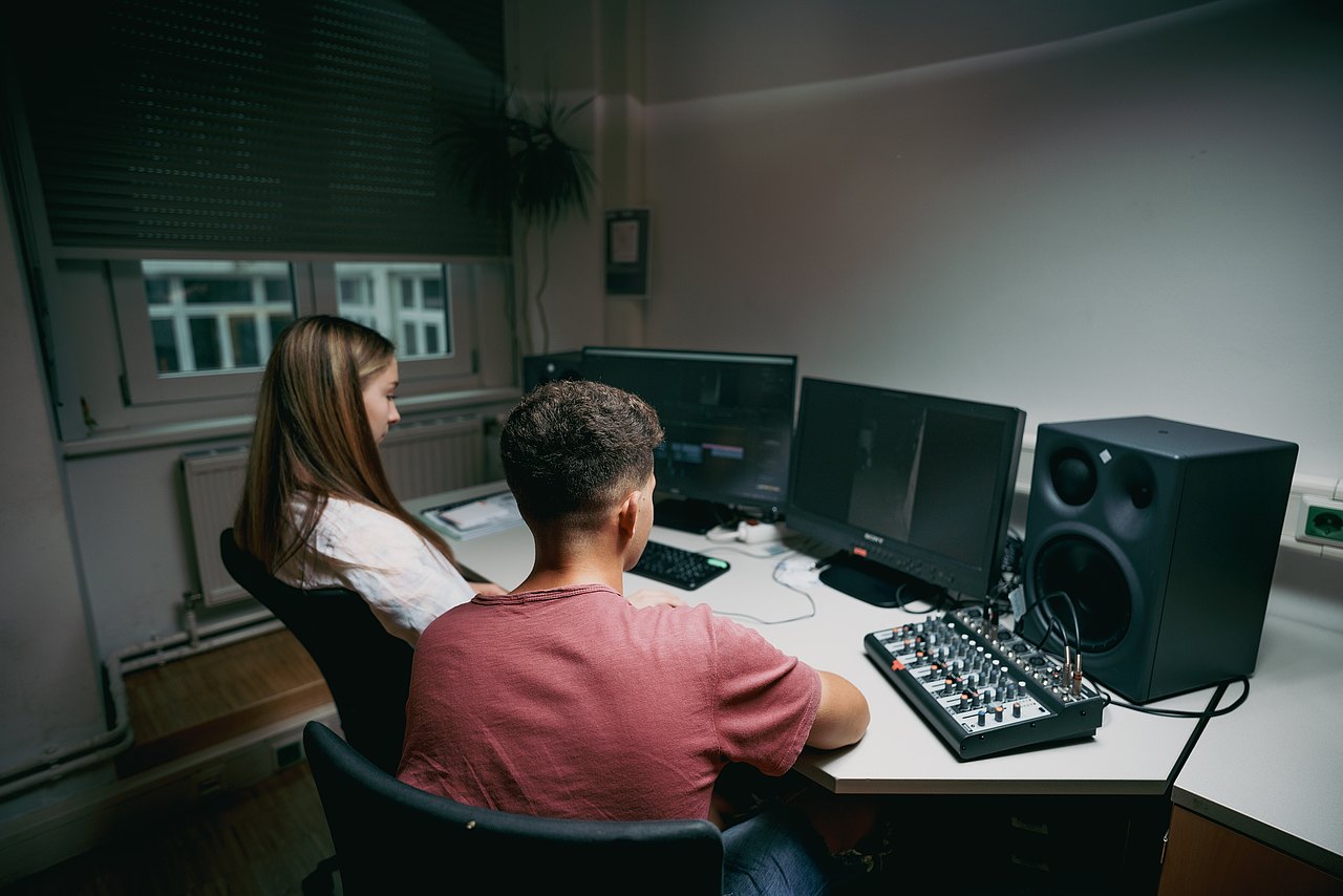 MZ_23_KRENN_v1-196 Zwei Jugendliche erstellen einen Filmschnitt vor zwei Computermonitoren.