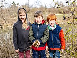 Drei Kinder stehen auf einem herbstlichen Feld.