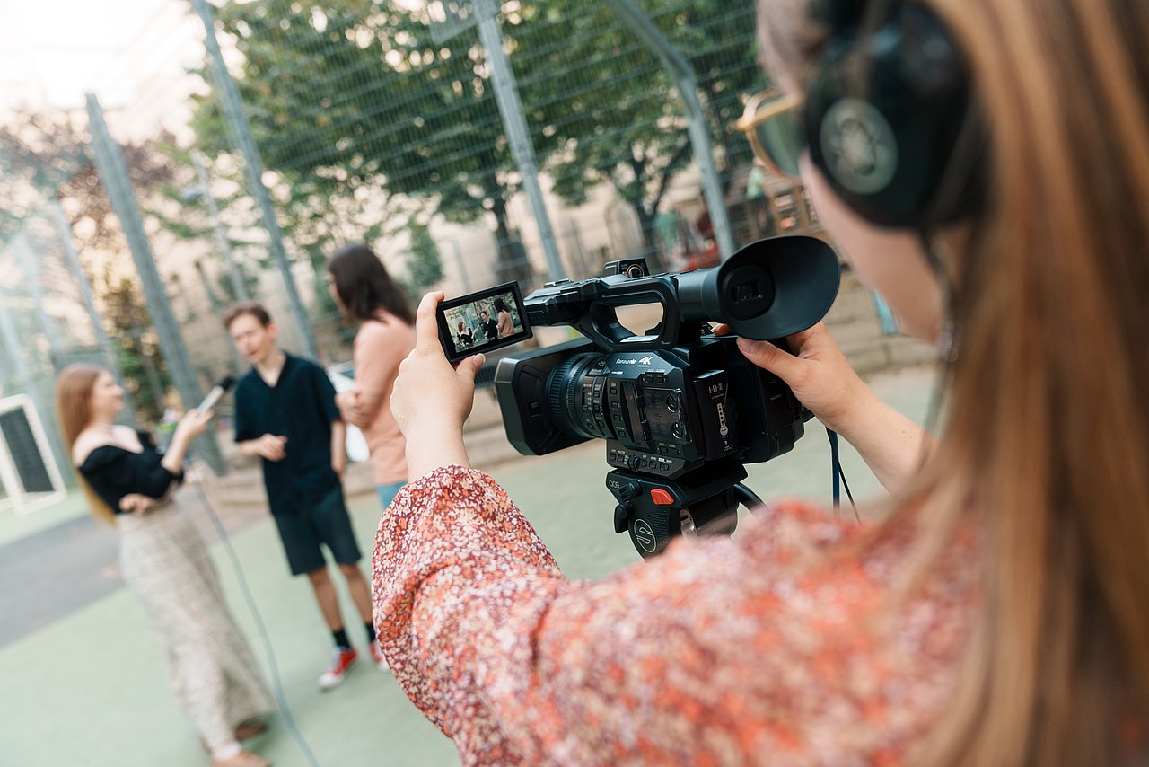 mz2025 x ste.krenn-187 Eine Jugendliche filmt drei andere Jugendliche mit einer Panasonic-Videokamera in einem Park.