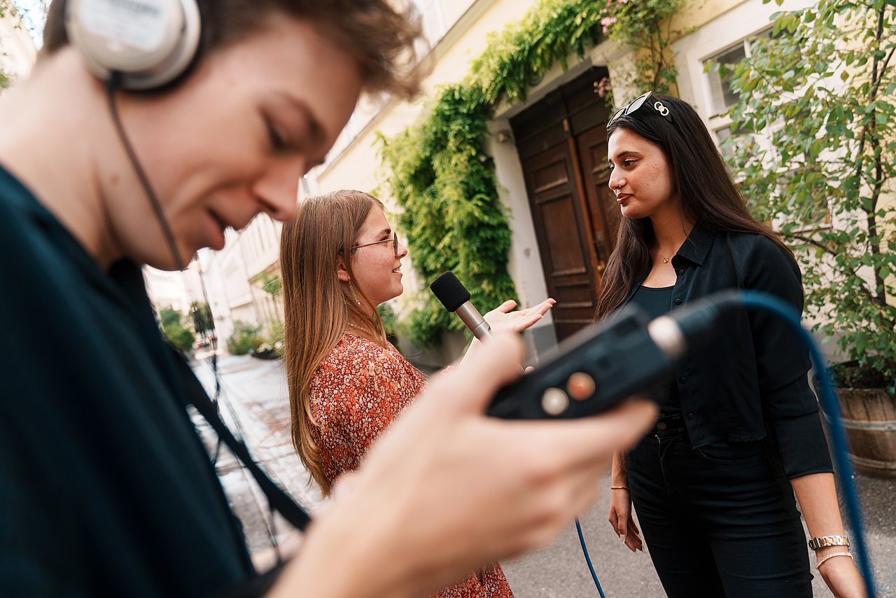 mz2025 x ste.krenn-197 Zwei Jugendliche führen ein Interview mit einem Mikrofon, während ein dritter Jugendlicher Kopfhörer und einen Audio-Recorder trägt