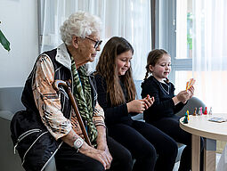EAW Schülerinnen spielen mit Pensionistin ein Kartenspiel.