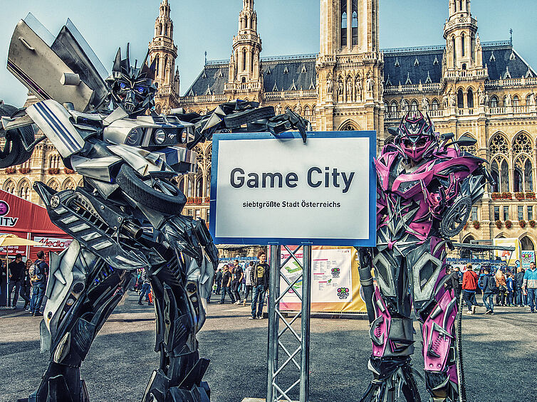 Überdimensionale Actionfiguren stehen vor dem Rathaus und halten ein Game City Ortsschild in die Höhe