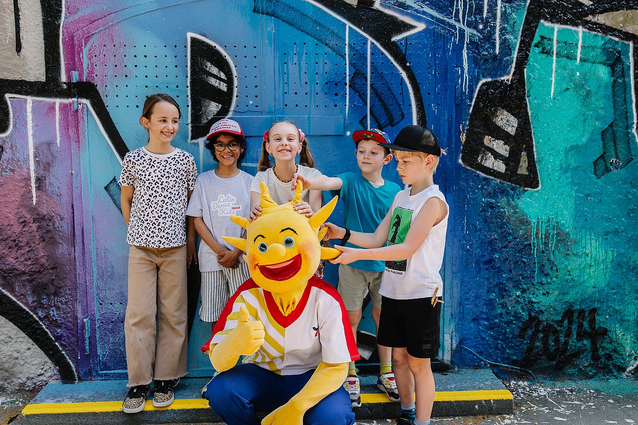 250606_MG_2127 Kinder mit dem Kinderaktivmaskottchen Holli vor einem Graffiti