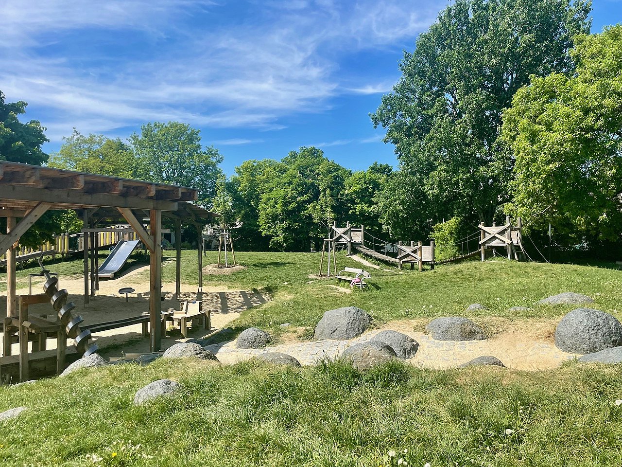 Spielplatz im Ingeborg-Bachmann-Park Wasserspielbereich mit Steinen und einer überdachten Sandkiste