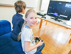 Mädchen blickt mit einem Controller in der Hand in die Kamera