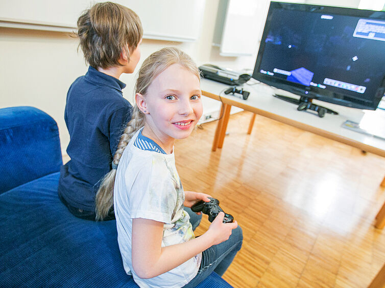 Mädchen blickt mit einem Controller in der Hand in die Kamera