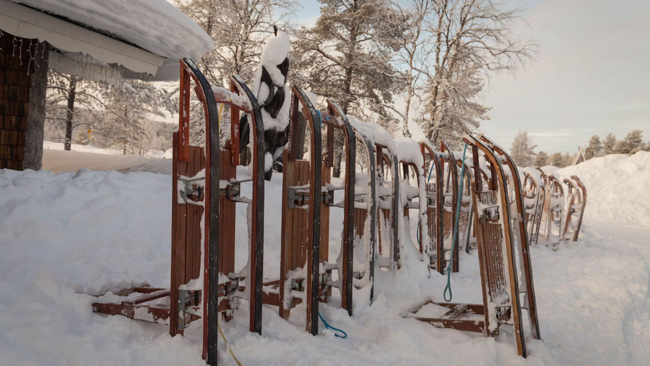 Alte Rodeln stehen im tiefen Schnee vor einem Gebäude in einer verschneiten Landschaft.