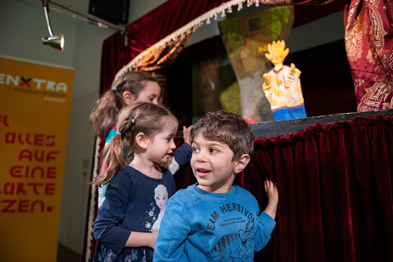 8679_© Barbara Mair Kinder stehen vor einer Puppentheaterbühne mit Holli-Puppe