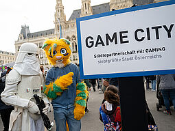 Zwei Cosplayer neben dem Game City Ortsschild
