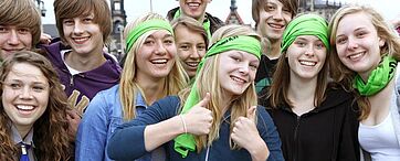 Gruppe von Jugendlichen lächelt in Kamera, teilweise mit grünen Schals und Stirnbändern