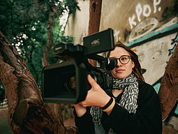 Junge Frau schaut durch eine Filmkamera.