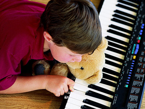 Musik Bub mit Teddy im Arm spielt Klavier