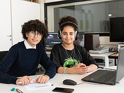 Frish. Jugendredaktion Zwei Jugendliche die an einem journalistischen Beitrag vor dem Laptop arbeiten, blicken freundlich.