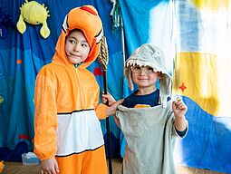 Zwei Kinder haben sich als Meerestiere verkleidet. Ein Kind ist ein Clownfisch und das andere ein Hai.
