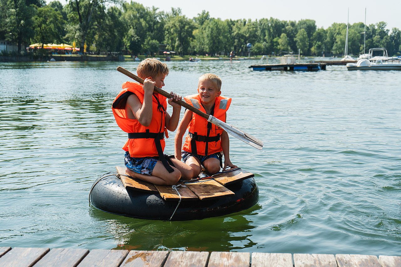 WIENXTRA_Ferienspiel_21072025_c_Kajetan_Koren_016 2 Kinder mit Schwimmwesten auf einem Floss im Wasser