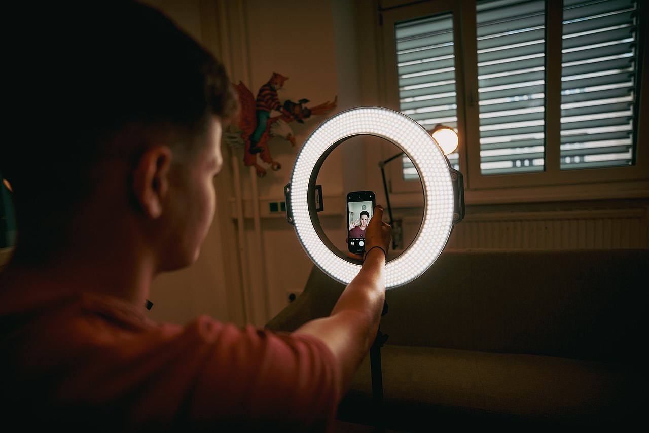 MZ_23_KRENN_v1-182 Ein Jugendlicher hält ein Smartphone vor einem LED-Ringlicht und filmt sich selbst.
