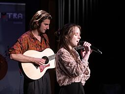 Ein Gitarrist und eine Sängerin machen Musik auf der Bühne.