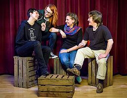 Vier junge Leute sitzen auf Holzkisten, sind lächelnd einander zugewandt