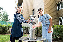 Wasserbrunnen Zwei Mädchen stehen am Wasserbrunnen
