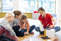 Bildungschancen Schülerinnen und Schüler blicken auf ein Haus aus Karton und erraten was sich darin befindet.