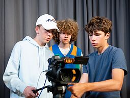 Frish. Jugendredaktion Drei Jugendliche stellen eine Videokamera ein bei einem Dreh.