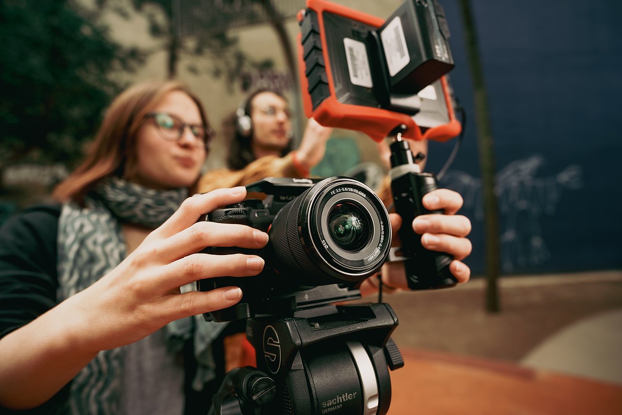 MZ_23_KRENN_v1-11 Eine Jugendliche bedient eine professionelle Sony-Kamera mit einem externen Monitor auf einem Stativ.