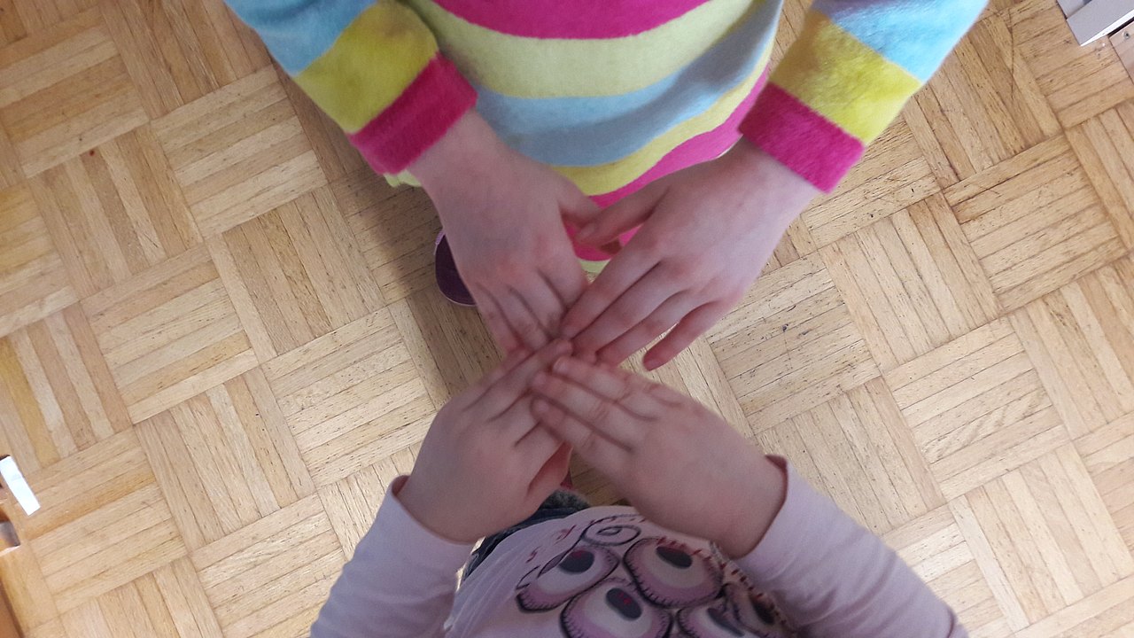 Klatschspiele Zwei Kinder haben die Fingerspitzen übereinander gelegt, sodass ihre Hände ein X ergeben.
