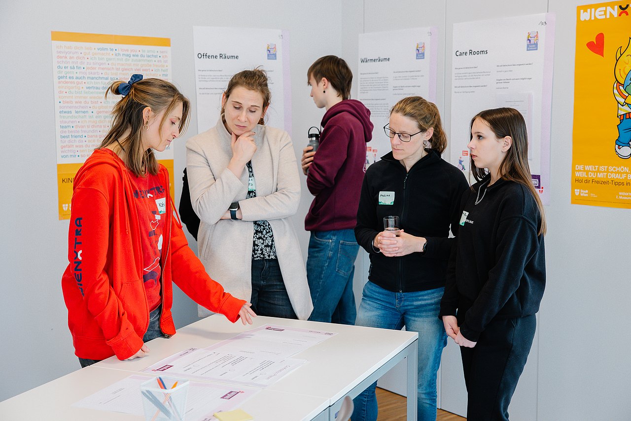 Junges Wien Personen stehen rund um einen Tisch und sprechen miteinander