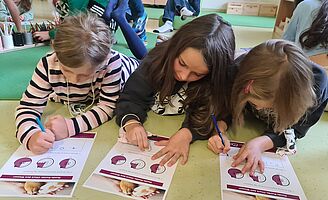 3 Kinder füllen, am Boden liegend, Fragebogen zu Hunde-Kunde aus