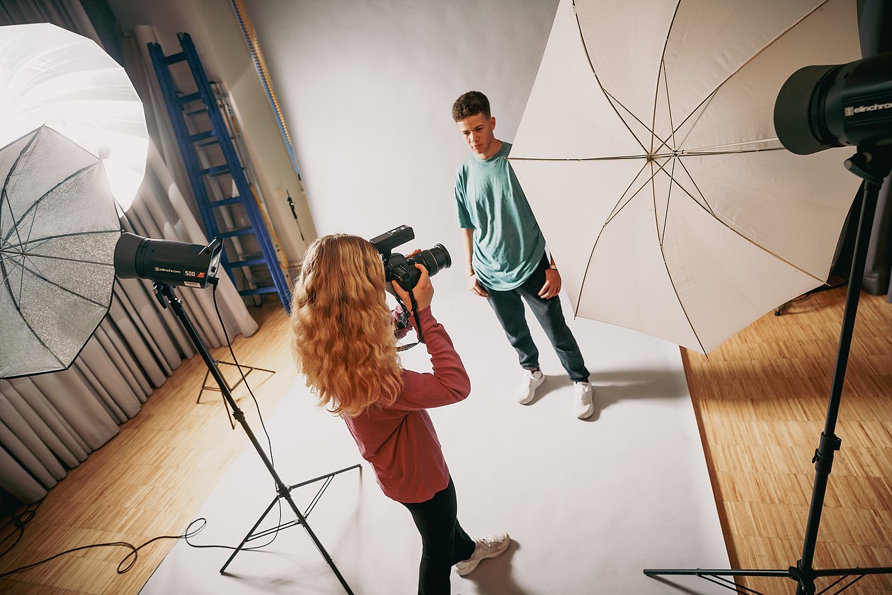 MZ_23_KRENN_v1-100 Eine Jugendliche fotografiert einen Jugendliche vor weißem Hintergrund in einem Studio.